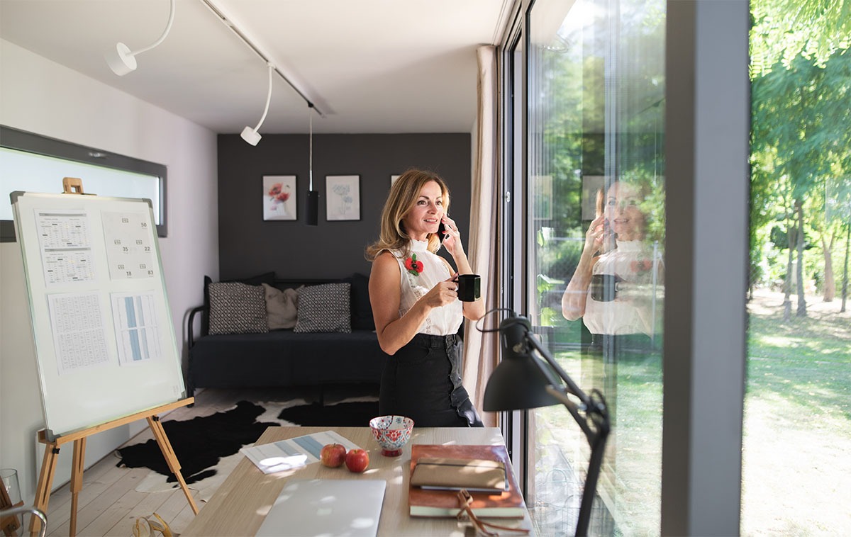 Mature woman working indoors in home office in office garden pod