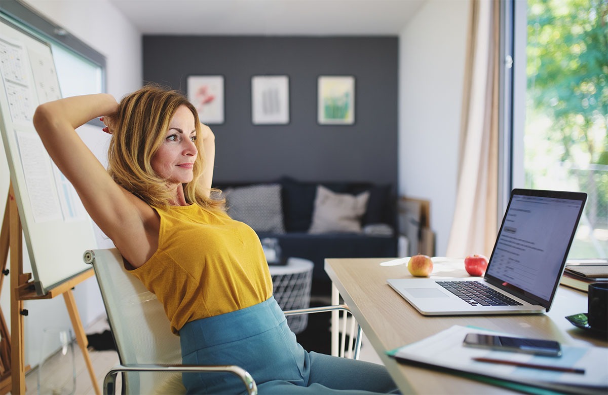 Mature woman working indoors in home office garden pod in container house in back garden.