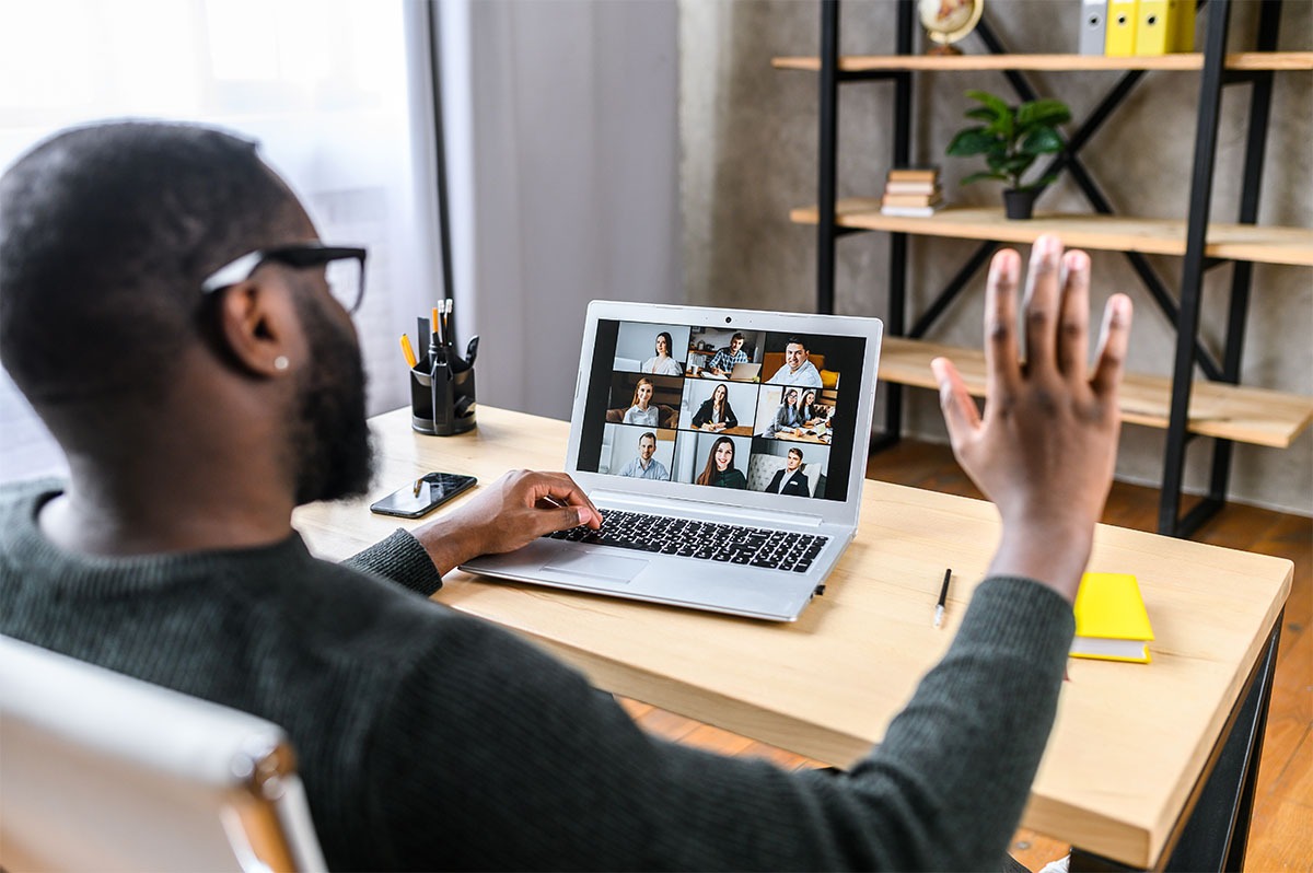 Confident African-American male worker talking online with coworkers, back view of black guy is waving hello to many people on video screen. Remote work, virtual meeting